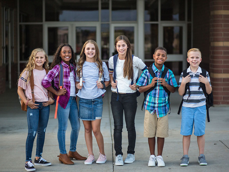 Group portrait of pre-adolescent school kids smiling in front of the school building
