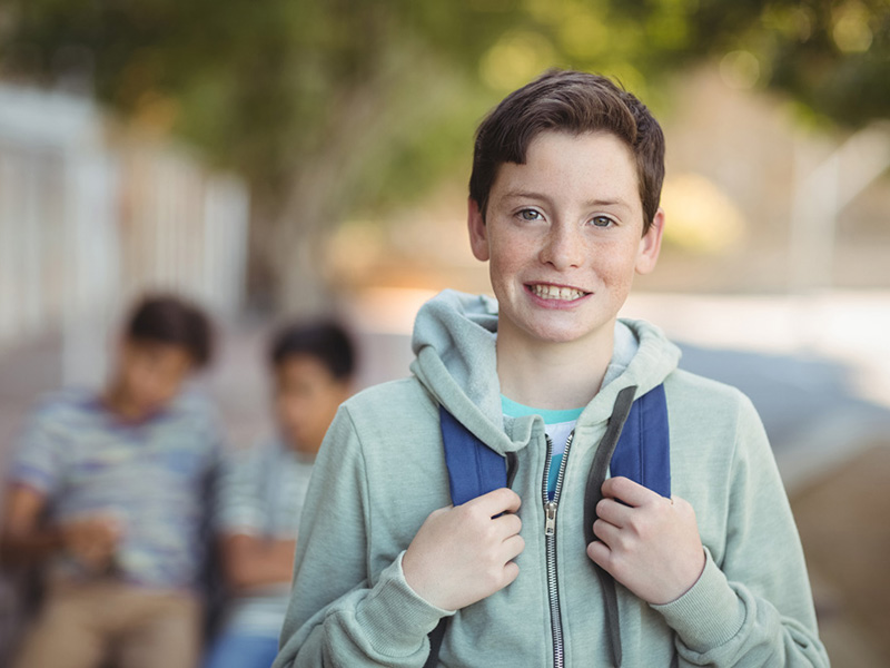 Smiling schoolboy standing with schoolbag in campus